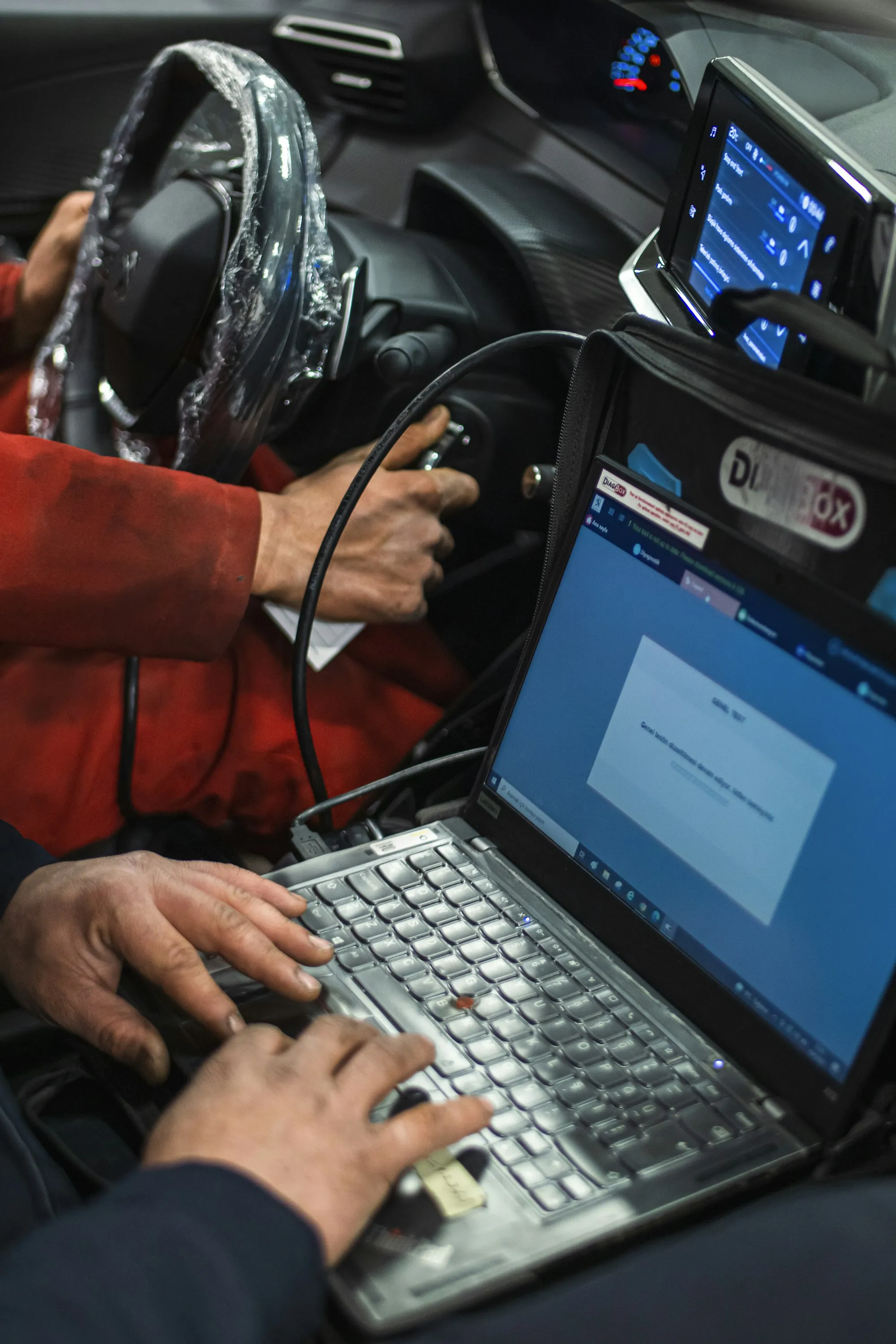 Person typing on a laptop placed under a car during diagnosis