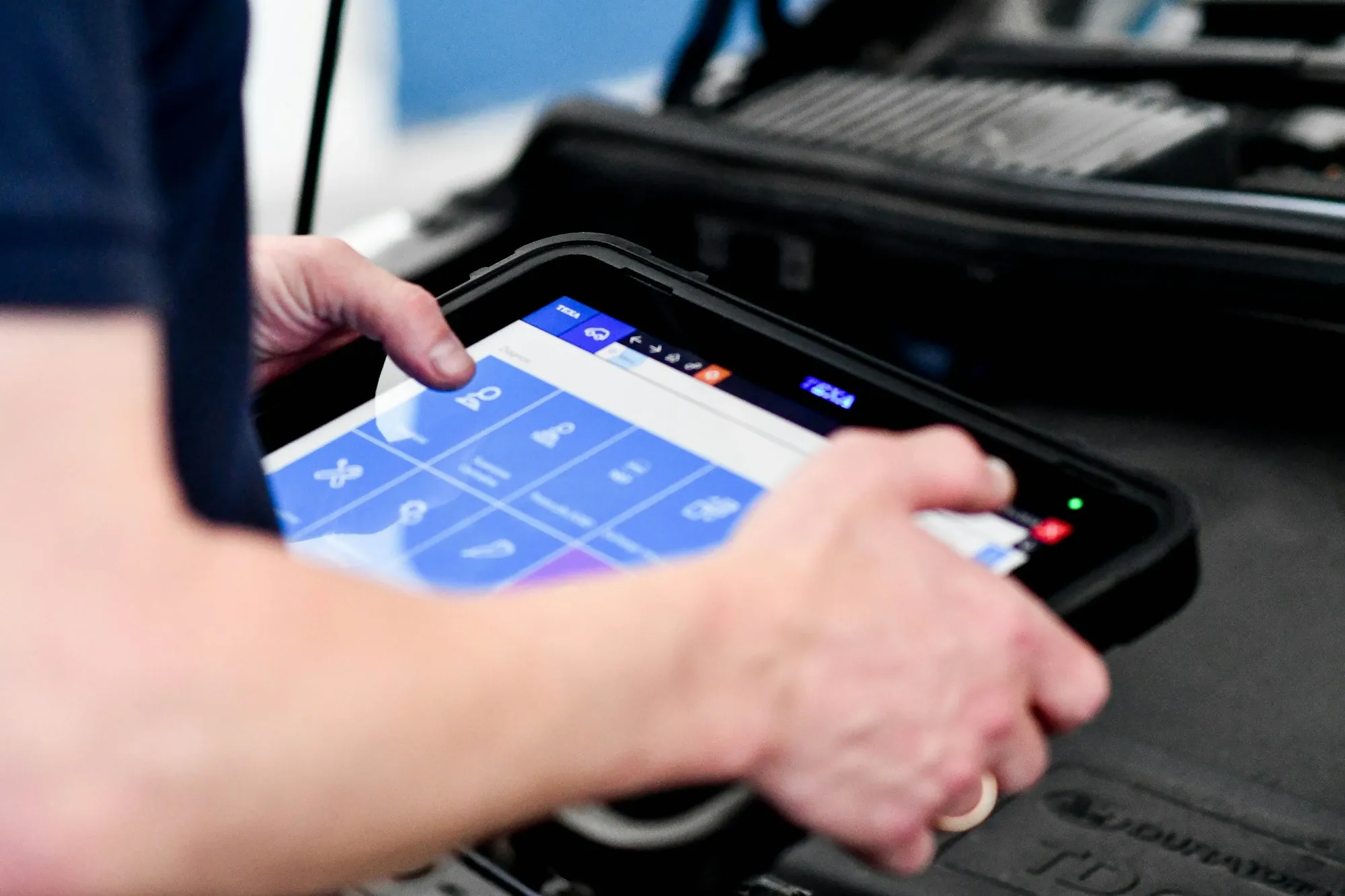 Hands holding a diagnostic tablet connected to a vehicle