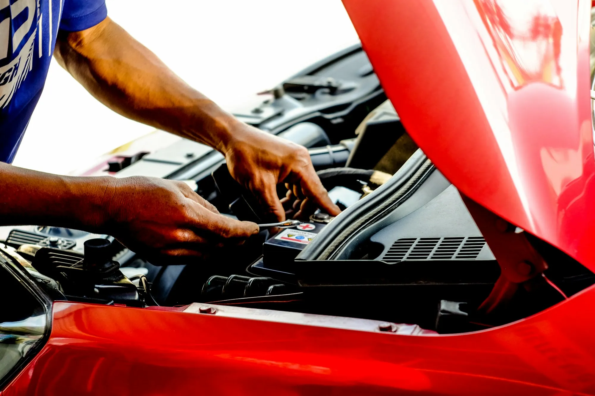 Two hands working inside the engine bay of a red car